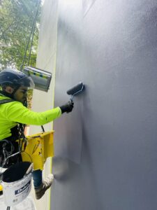 Rope access technician applying a coating to a building exterior