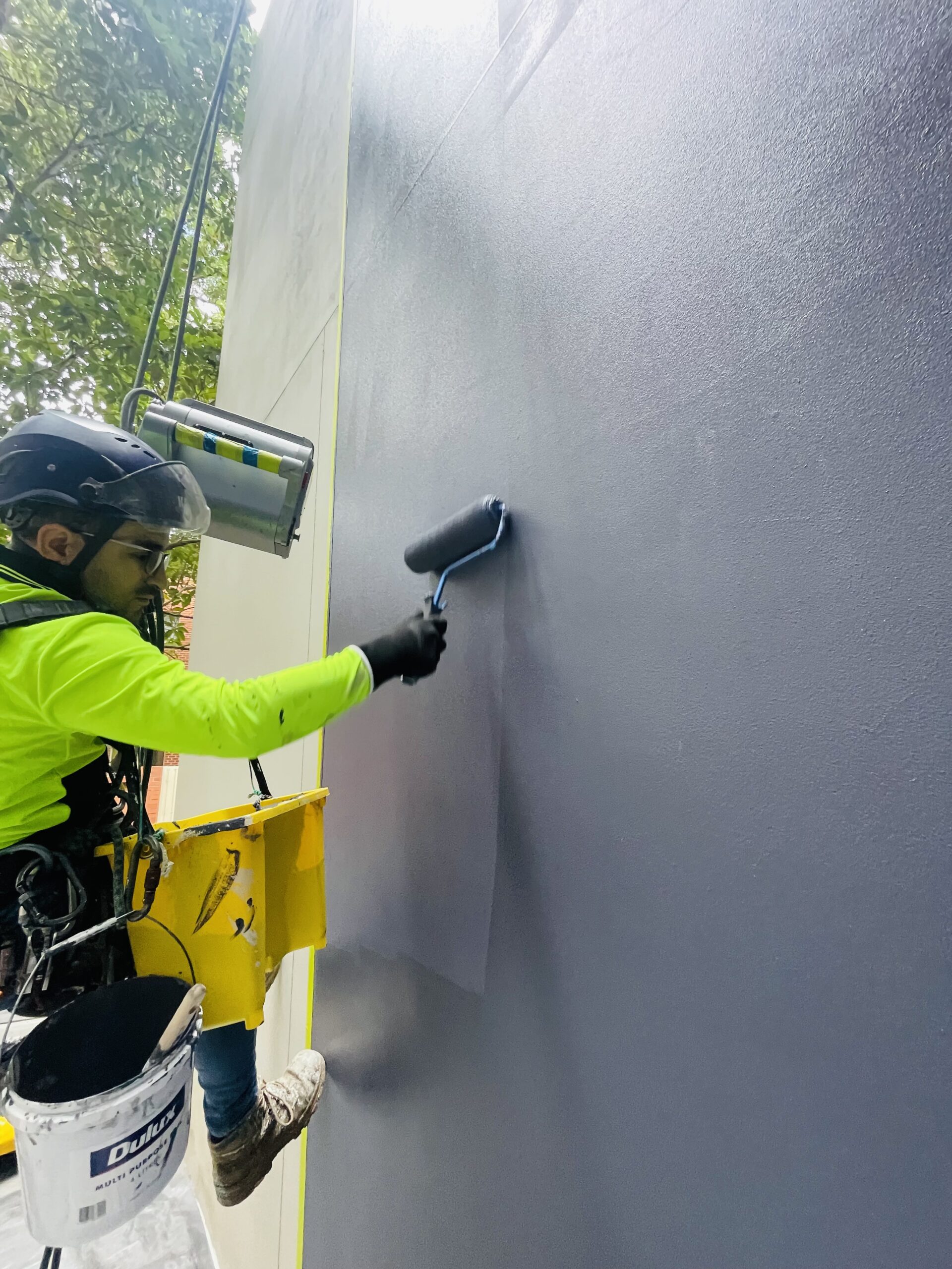 Rope access technician applying a coating to a building exterior